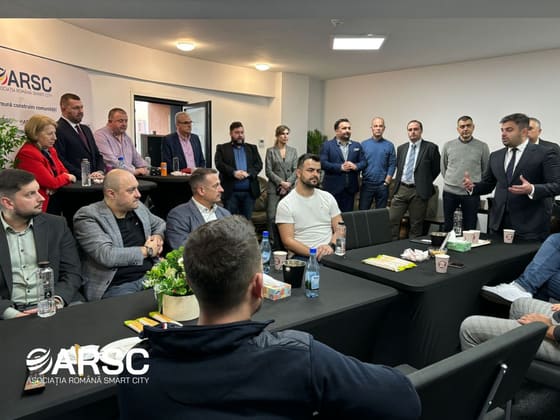 Grup de participanți adunat în jurul gazdei, care vorbește în picioare.