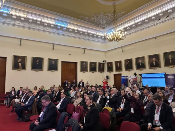 Sală cu public așezat, într-o încăpere cu tablouri pe pereți.