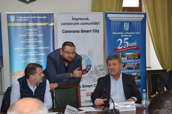 Masă rotundă cu prezidiu și participanți, într-o sală de consiliu.