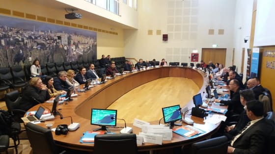Sală mare cu masă în formă de U, plină de participanți.