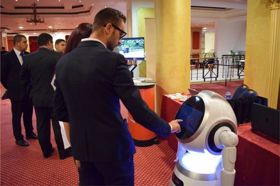 Participant atingând ecranul unui robot de serviciu, lângă un stand.