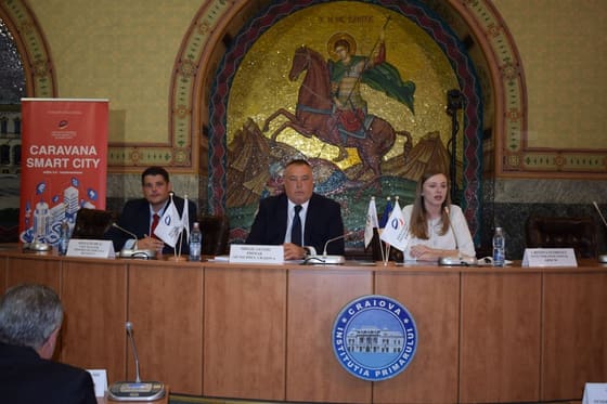 Prezidiu într-o sală de consiliu, cu stema instituției pe perete.