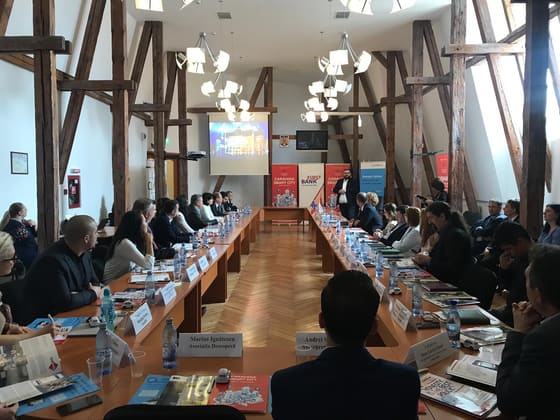 Prezentare într-o sală cu grinzi de lemn, cu public așezat.