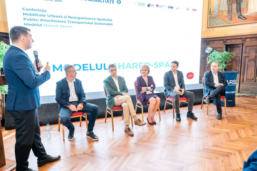 Panel de cinci invitați pe scenă, moderator în picioare cu microfonul.