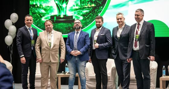 Grup de participanți pe scenă, în fața unui ecran verde.