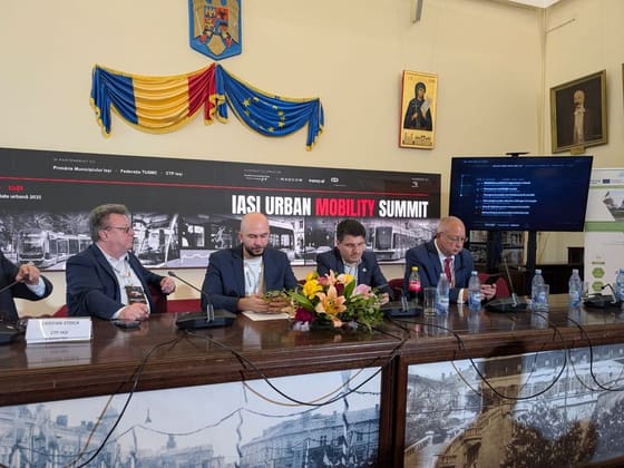 Prezidiu cu patru vorbitori, într-o sală istorică cu drapele.