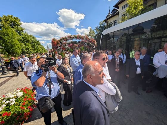 Grup de participanți cu ecusoane, în stradă, lângă un vehicul de transport public.