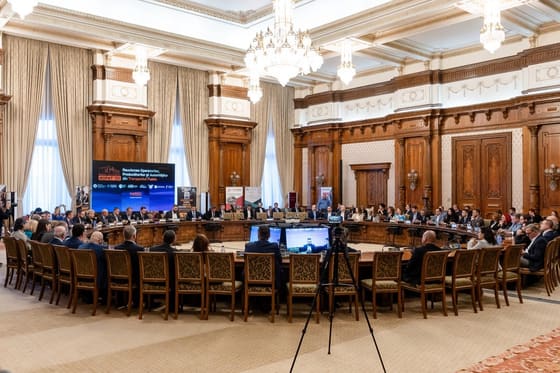 Sală mare cu masă în formă de U, plină de participanți.