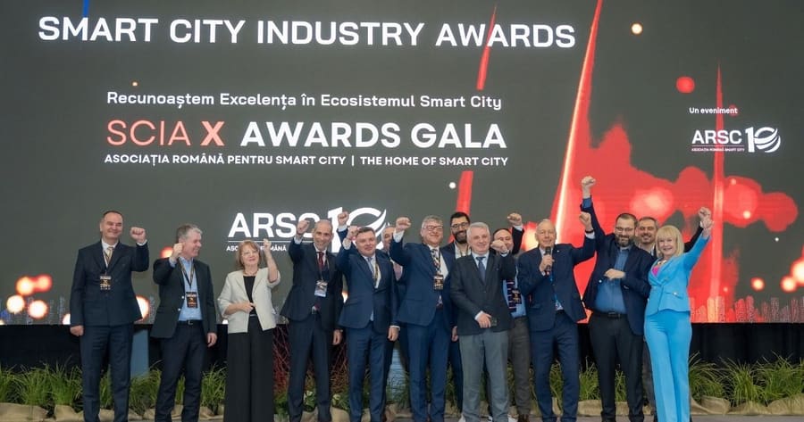 Grup de premianți pe scenă, cu brațele ridicate, în fața ecranului Smart City Industry Awards.